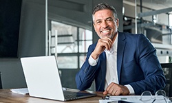 Senior man smiling and sitting at desk with laptop