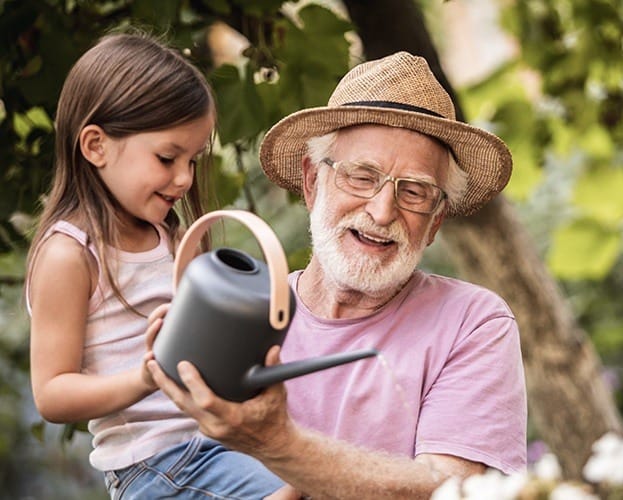 Older man with dental implant tooth replacement holding his grandchild