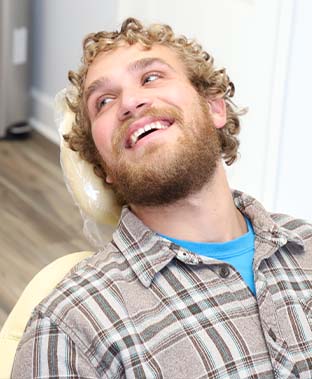 Man with curly blond hair smiling in dental chair