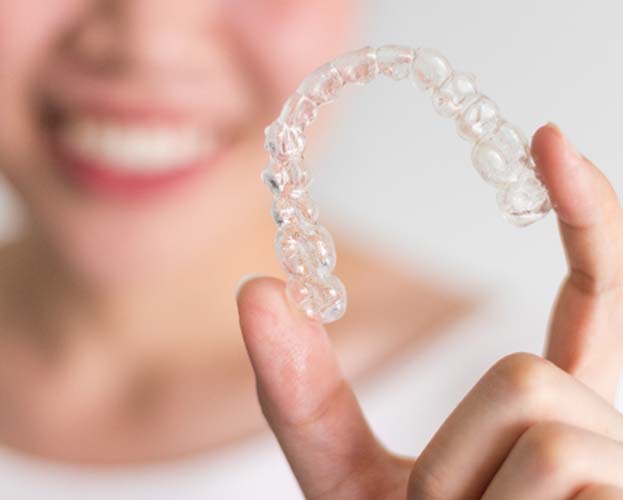 Woman smiling while holding up Invisalign in Leesburg