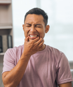 Man in pink shirt squinting and touching corners of mouth in pain