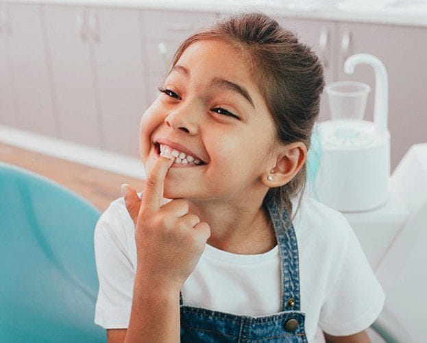 Little girl pointing to smile after tooth colored filling treatment