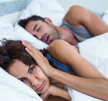 Frustrated woman sleeping next to snoring man in need of sleep apnea therapy