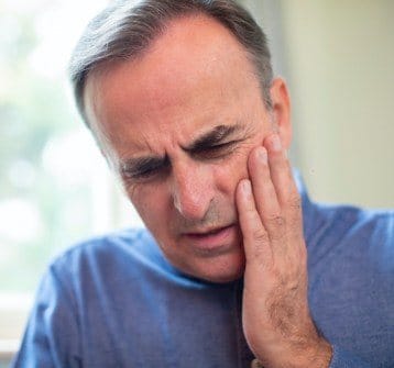 Man in need of emergency dentistry holding cheek in pain