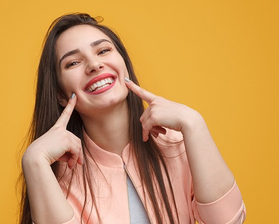 woman smiling and pointing at her porcelain veneers in Leesburg