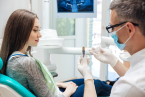 Dentist holding a model dental implant during consultation with patient