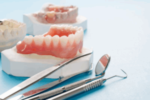 Dentures sitting on a blue surface next to several dental tools