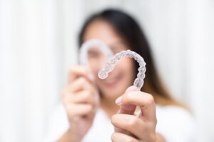 Woman smiling while holding her Invisalign trays
