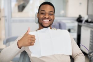 Man at the dentist smiling and holding thumbs up