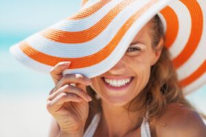 Woman happily smiling while partly covering her face with a hat.